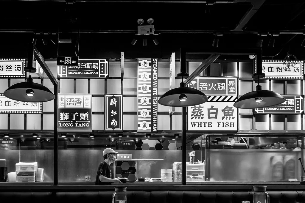 The counter of a small Chinese restaurant with a wall of hanging menu boards above it, dish names set mostly in Chinese characters.